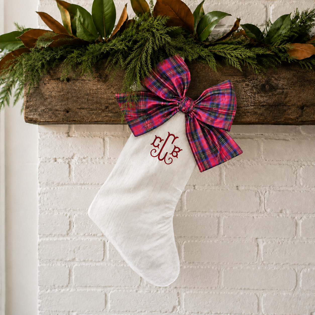 Personalized ivory silk Christmas stocking with red tartan bow styled on a holiday mantel